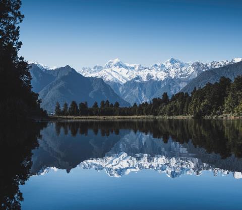 March 2021 photo writing prompt (photo of placid lake surface reflecting trees and snowcapped mountains in background)