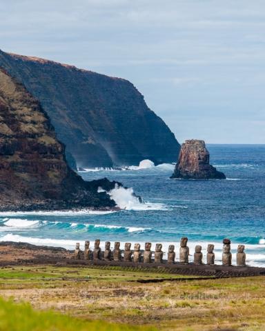 rocky seashore with waves before a row of stone figures via Canva
