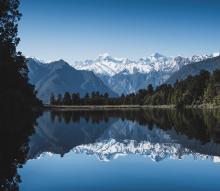 March 2021 photo writing prompt (photo of placid lake surface reflecting trees and snowcapped mountains in background)